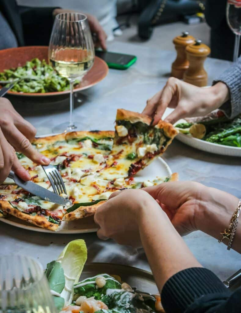 Personer delar en pizza med sallad och vitt vin.