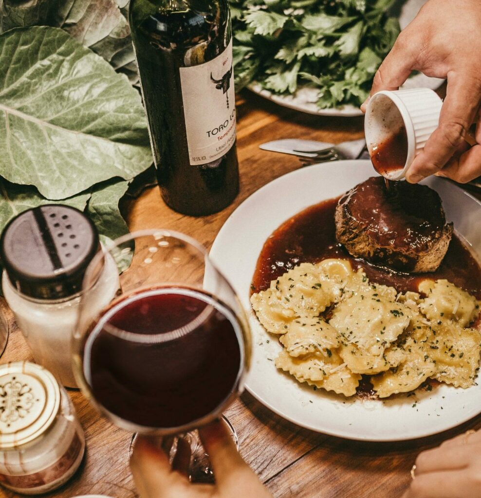 Rött vin tillsammans med en måltid och ingredienser på ett bord.