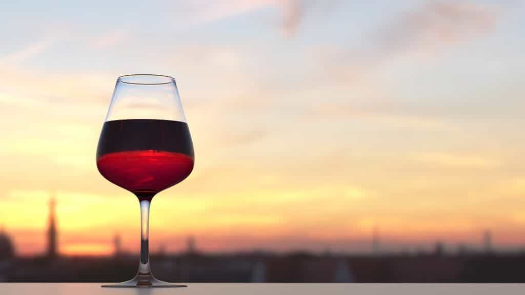 Ett glas Nebbiolo Barolo vin med solnedgång i bakgrunden.