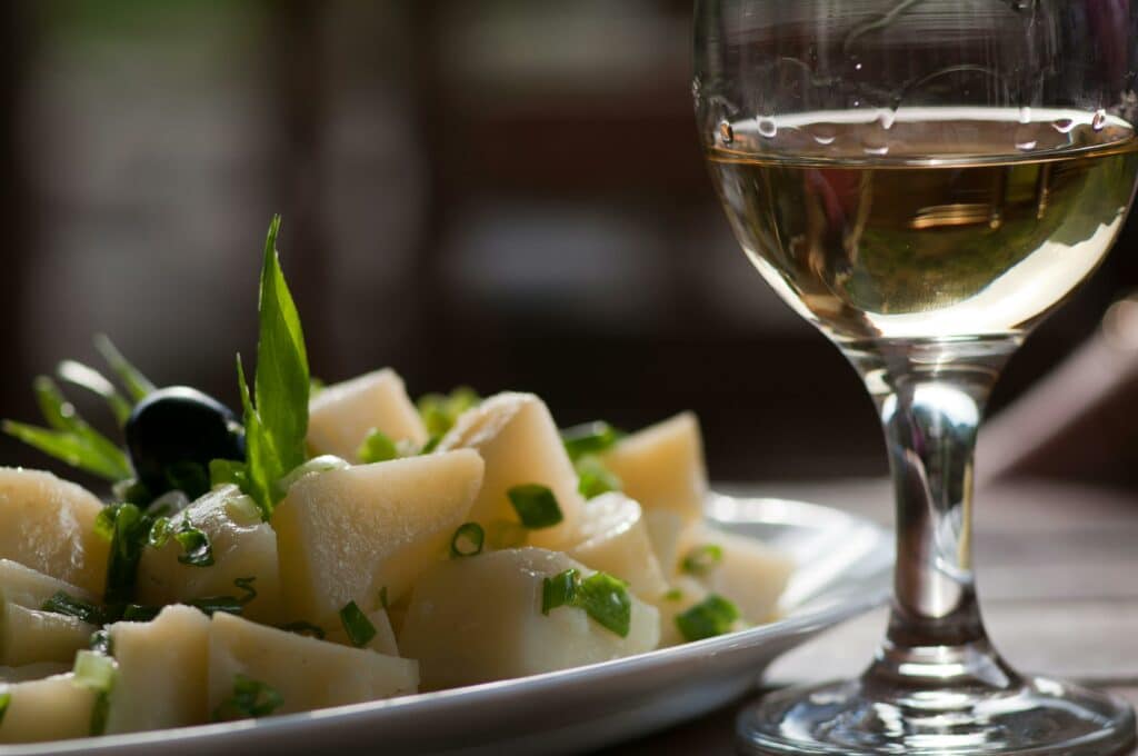 Närbild på ett glas Rieslingvin tillsammans med en maträtt av pasta och grönsaker.